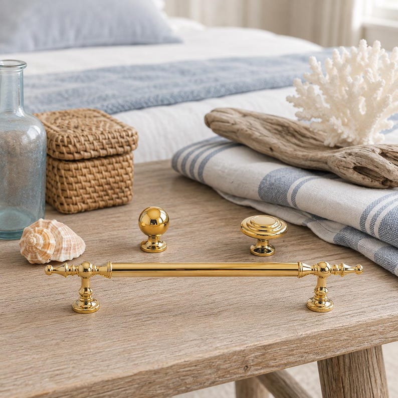 May include: A set of three polished gold-tone metal hardware pieces consisting of one long horizontal cabinet pull with decorative finials, one spherical knob, and one flat circular knob with concentric ring detailing on the top surface.