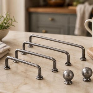 May include: A set of three dark gray metal drawer pulls with a weathered finish and two matching round cabinet knobs. The pulls feature a long, arched bar design with circular mounting bases at each end, while the knobs have a spherical shape.