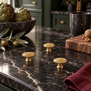 May include: Three round, gold-toned metal cabinet knobs featuring a detailed, embossed floral pattern on the top surface. Each knob has a tapered base and a textured, decorative edge, presented as a set of hardware for furniture or cabinetry.