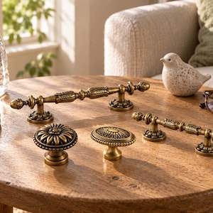 May include: A collection of four antique brass hardware pieces including two elongated drawer pulls with ornate detailing and two round cabinet knobs, one featuring a floral petal design and the other an oval textured pattern with beaded edges.