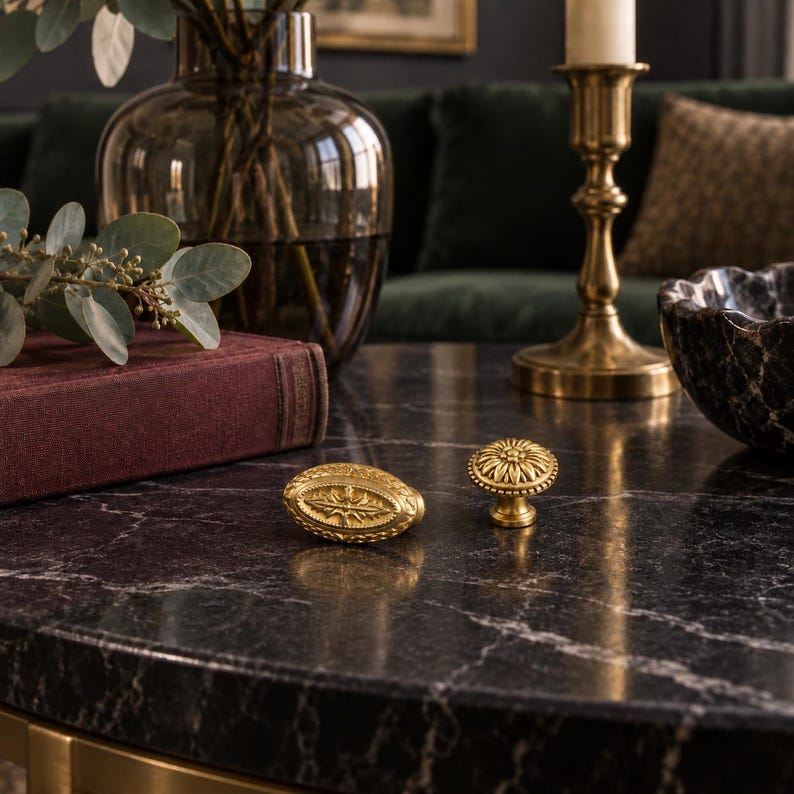 May include: Two brass-toned metal cabinet knobs with intricate relief detailing. One knob is oval-shaped with a central star-like motif, while the other is circular with a radial floral pattern. Both feature a textured, antique-style finish.