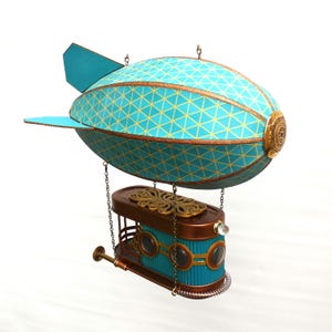 May include: A decorative steampunk-style airship model. The teal airship body features a yellow geometric pattern and bronze accents. The gondola below is teal and bronze with circular windows and decorative elements. A unique, whimsical decor item.