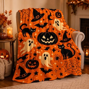 May include: An orange throw blanket featuring a repeating Halloween pattern of black witch hats, jack-o'-lanterns, black cats, white ghosts, bats, spiders, and spiderwebs, with small black stars and diamond shapes scattered across the fabric.