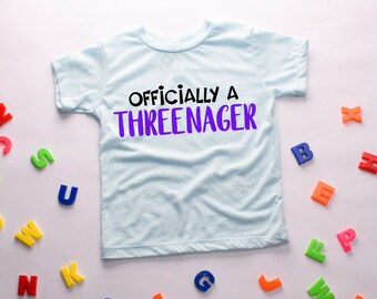 Könnte beinhalten: Ein hellblaues T-Shirt mit dem Text "Officially a Three-nager" in schwarzen und violetten Buchstaben.