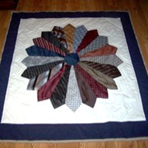 May include: A white quilt with a navy blue border. The centre of the quilt is made up of a circular pattern of tie-shaped fabric pieces in various colours and patterns.