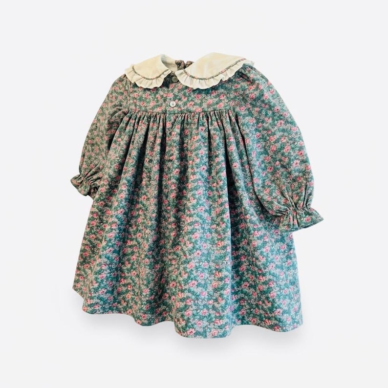 Puede incluir: Vestido verde con estampado floral, mangas largas y cuello blanco. El vestido presenta un escote redondo y una falda fruncida. Las mangas tienen pu&ntilde;os con volantes. El estampado floral incluye flores rosas.