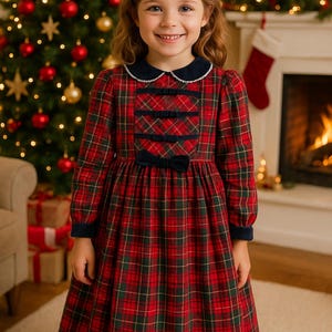 May include: A young girl wearing a red, green, and gold plaid dress with a navy blue collar and cuffs. The dress features decorative bows and is set against a Christmas tree and fireplace background.