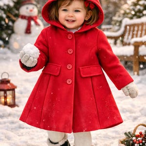 May include: A young child wearing a bright red hooded coat with matching buttons, standing in the snow. The coat has a flared skirt and is paired with white leggings and black boots. The scene is set in a snowy winter landscape.