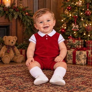 May include: A short-sleeved red velvet romper with a white collar and white trim on the sleeves. The romper features two small white buttons on the chest. The outfit is paired with white knee-high socks and white leather baby shoes.