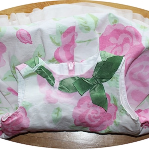 May include: A white sleeveless dress with a pink rose print and a green bow at the neckline.