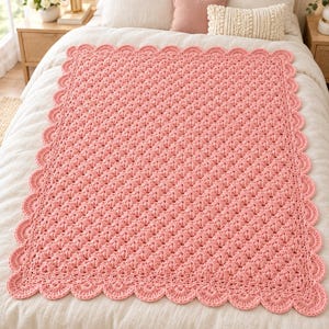 May include: A rectangular crochet blanket in a solid light pink color. The blanket features a repeating shell stitch pattern throughout the center and is finished with a decorative scalloped edge border that frames the entire piece.