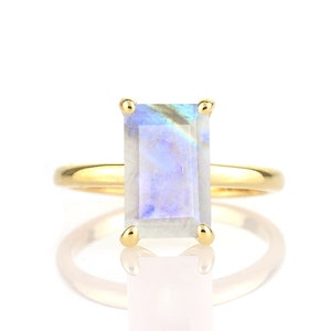 May include: A gold ring with a rectangular iridescent gemstone. The gemstone has a blue and white color.