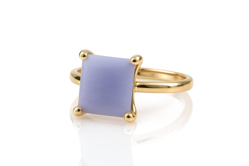 May include: A gold ring with a square, lavender-colored gemstone set in a prong setting.