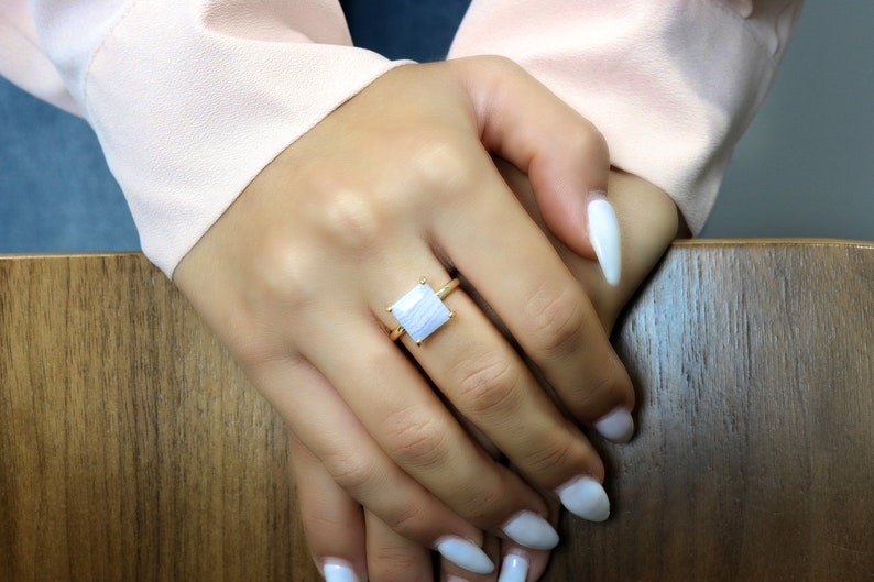 May include: A gold ring with a square white agate gemstone. The ring is on a person's finger.