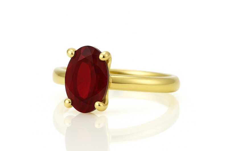 May include: A gold ring featuring a large, oval-cut, deep red gemstone. The gemstone is held in place by four gold prongs. The ring band is a smooth, polished gold.