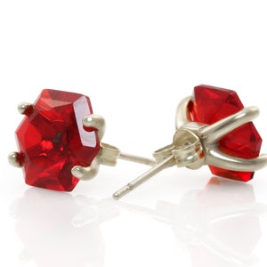 May include: A pair of silver earrings with red gemstone accents. The gemstones are faceted and have a hexagonal shape.