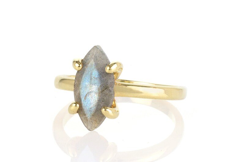 Puede incluir: Un anillo de oro con una piedra preciosa de labradorita con corte marquesa. La piedra iridiscente gris y azul est&aacute; sujeta por cuatro garras de oro. La banda del anillo es de oro pulido simple.
