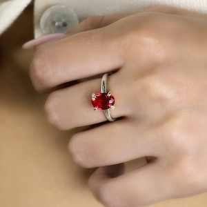 May include: A silver ring with a large oval-shaped red gemstone.