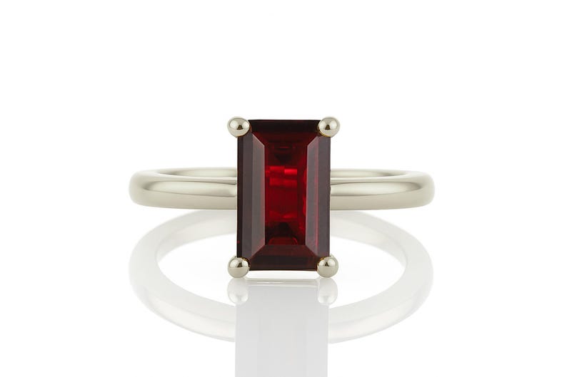 May include: A silver ring with a red rectangular gemstone set in a bezel setting.