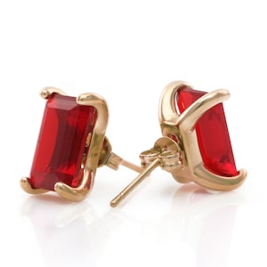 May include: A pair of gold earrings with red gemstone studs. The earrings have a simple design and are perfect for everyday wear.