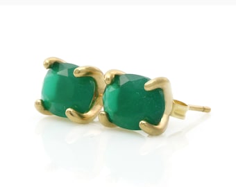 Puede incluir: Un par de pendientes de oro con piedras preciosas facetadas de color verde esmeralda. Las piedras están sujetas por cuatro garras de oro. Se presentan sobre un fondo blanco.