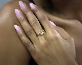 May include: A gold ring with a pear-shaped pink gemstone. The ring is on a person's finger.