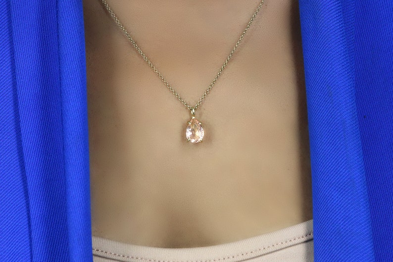 May include: A gold chain necklace with a pear-shaped pink gemstone pendant.