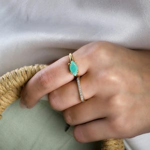 K&ouml;nnte beinhalten: Zwei goldene Ringe an einer Hand. Der obere Ring hat einen t&uuml;rkisfarbenen, markisenf&ouml;rmigen Stein. Der untere Ring ist ein d&uuml;nnes Band mit kleinen Diamanten.