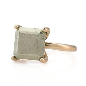 Puede incluir: Un anillo de oro con una piedra cuadrada de color gris claro.