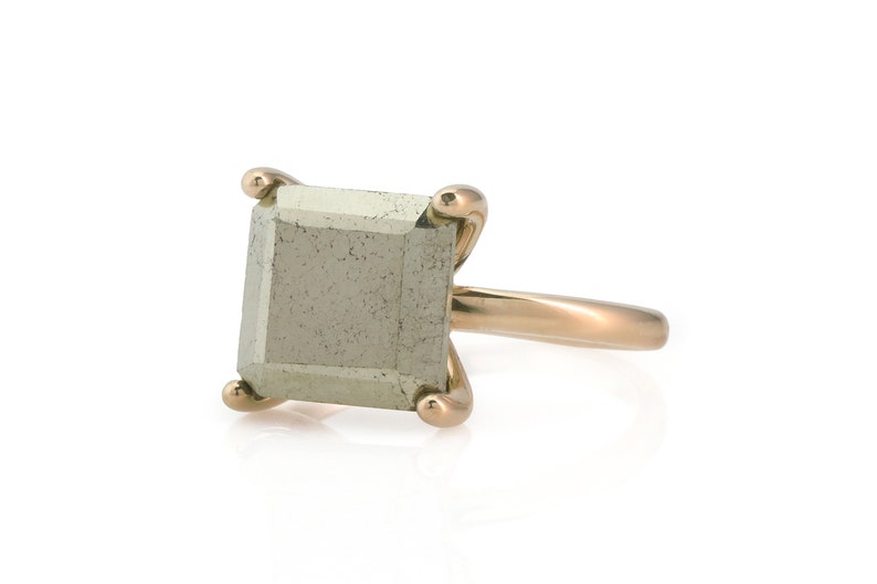 Puede incluir: Un anillo de oro con una piedra cuadrada de color gris claro.