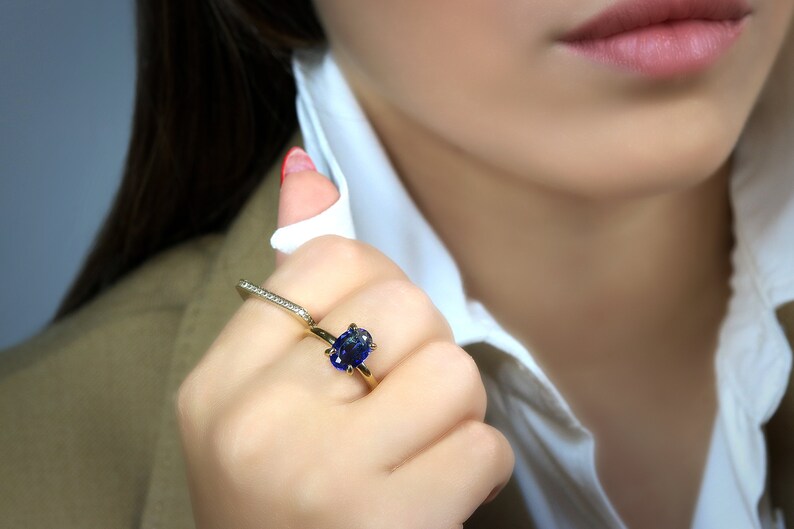Op de afbeelding: Een gouden ring met een grote blauwe ovale edelsteen in een kraalbezetting. De ring wordt gedragen aan de wijsvinger.