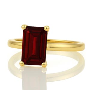 May include: A gold ring with a large, rectangular, dark red gemstone.