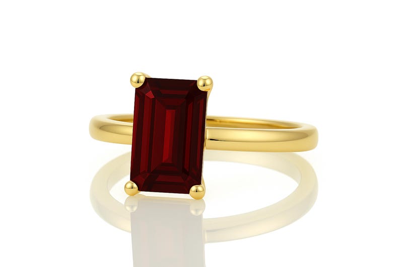 May include: A gold ring with a large, rectangular, dark red gemstone.