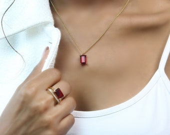 Puede incluir: Un collar de cadena de oro con un colgante de piedra rectangular roja. El collar lo lleva una persona con una camisa blanca. La persona también lleva un anillo de oro con una piedra rectangular roja.