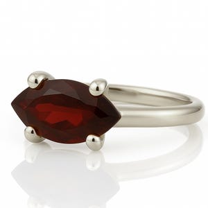 May include: A silver ring with a marquise-shaped red gemstone set in the center. The ring has four small silver accents on the band.