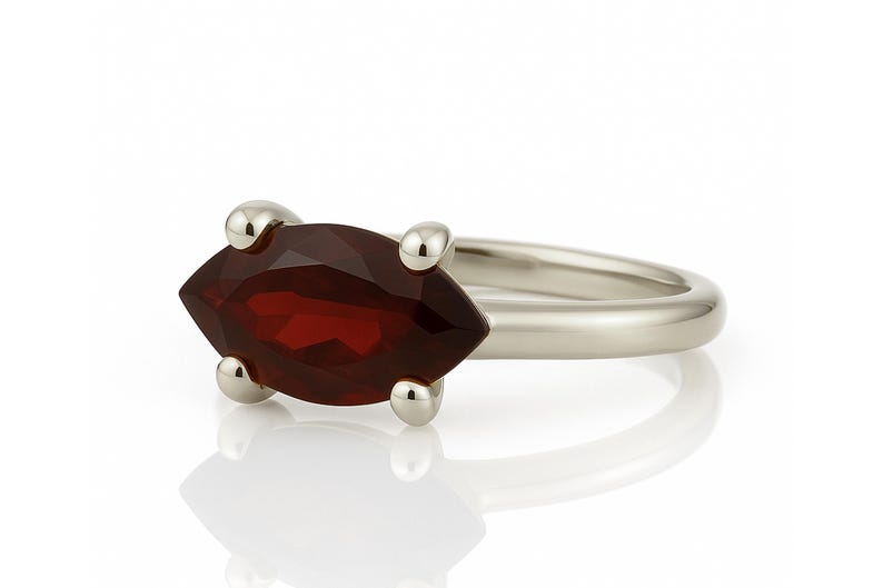 May include: A silver ring with a marquise-shaped red gemstone set in the center. The ring has four small silver accents on the band.