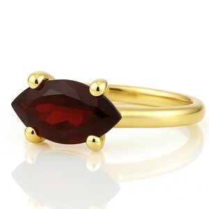 May include: A gold ring with a marquise-shaped garnet gemstone. The ring is set with four small gold balls on each side of the stone.