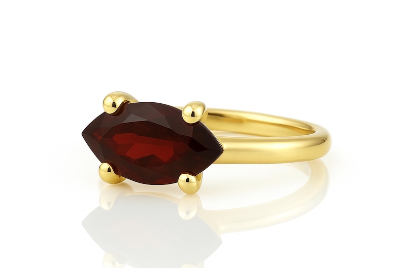 May include: A gold ring with a marquise-shaped garnet gemstone. The ring is set with four small gold balls on each side of the stone.