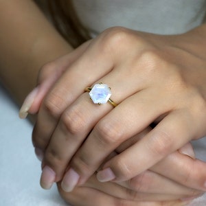 May include: A gold ring with a hexagonal moonstone gemstone. The ring is on a person's finger.