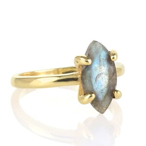 Puede incluir: Un anillo de oro con una piedra preciosa de labradorita en forma de marquesa. La piedra iridiscente azul-gris est&aacute; sujeta por cuatro garras de oro. La banda del anillo es de oro liso y pulido.