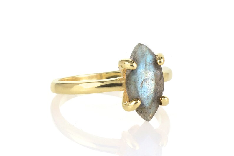Puede incluir: Un anillo de oro con una piedra preciosa de labradorita en forma de marquesa. La piedra iridiscente azul-gris est&aacute; sujeta por cuatro garras de oro. La banda del anillo es de oro liso y pulido.