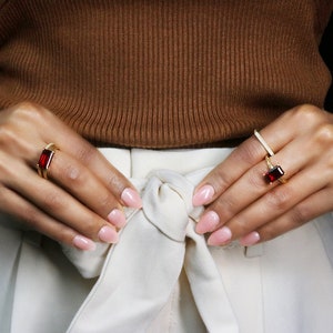 May include: Two gold rings with red gemstones. The rings are worn on the index and middle fingers of a person's hand.
