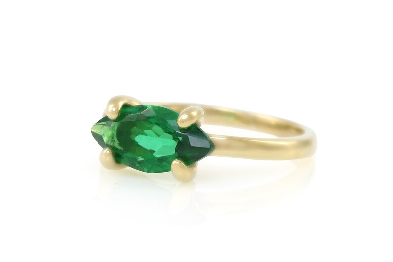 Puede incluir: Un anillo de oro con una piedra preciosa verde en forma de marquesa.