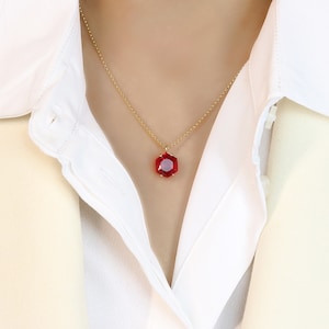 以下が含まれることがあります： 赤い宝石のペンダントが付いたゴールドチェーンネックレス。ペンダントはファセットカットの八角形です。