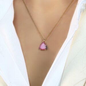 May include: A gold chain necklace with a pink triangular pendant featuring a pink and white gemstone.