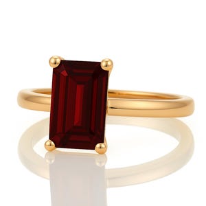 May include: A gold ring with a large, rectangular, dark red gemstone.