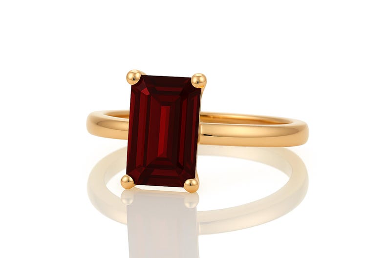 May include: A gold ring with a large, rectangular, dark red gemstone.