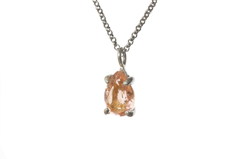 May include: A silver chain necklace with a pear-shaped pendant featuring a light pink and orange gemstone.