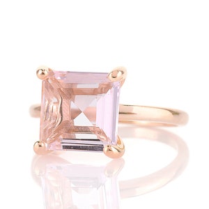 May include: A gold ring with a large, square-shaped, light pink gemstone.