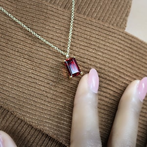 May include: A gold chain necklace with a red rectangular gemstone pendant.